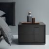 Dark grey bedside table with modern graphic handles in a minimalist bedroom